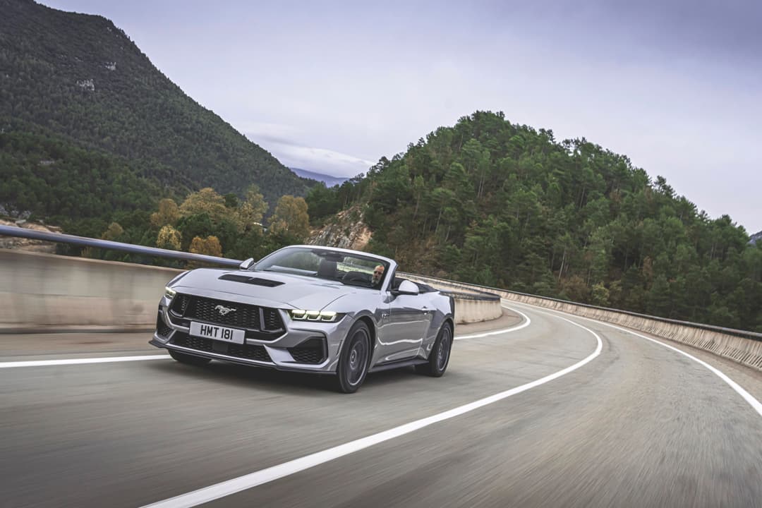 Ford Mustang Dark Horse décapotable blanc en virage sur une route de montagne
