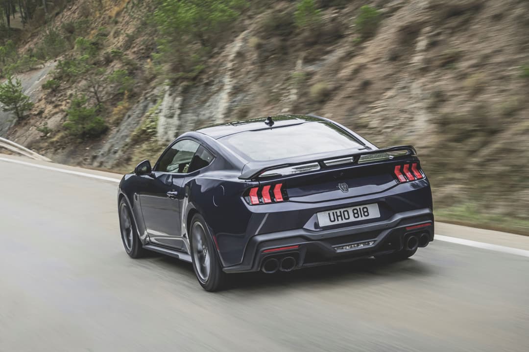 Nouvelle Ford Mustang noire en courbe sur route de montagne, vue de trois quarts arrière montrant l'aileron et les feux arrière