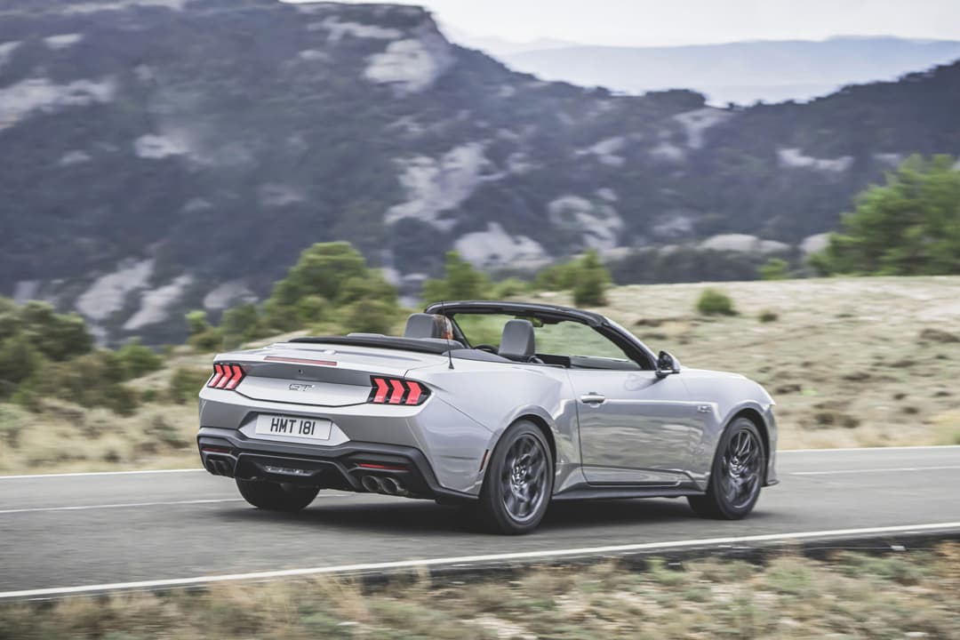 Ford Mustang convertible blanche en conduite sur route de montagne, vue de trois quarts arrière