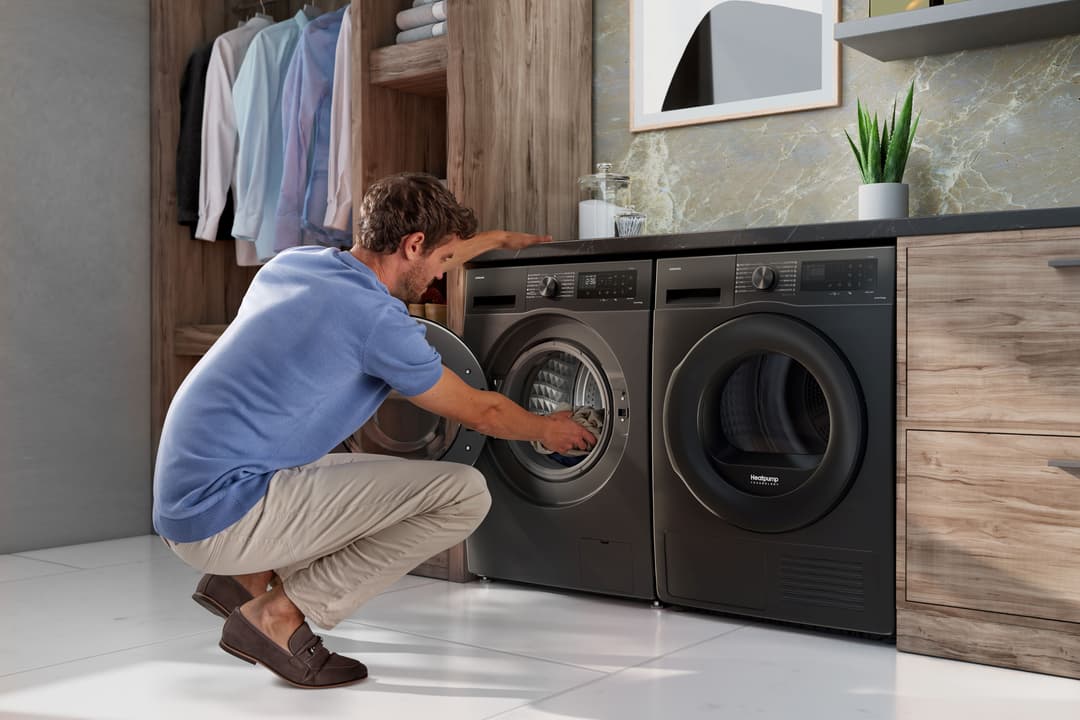 Homme en tee-shirt bleu chargeant une machine à laver noire dans une buanderie moderne