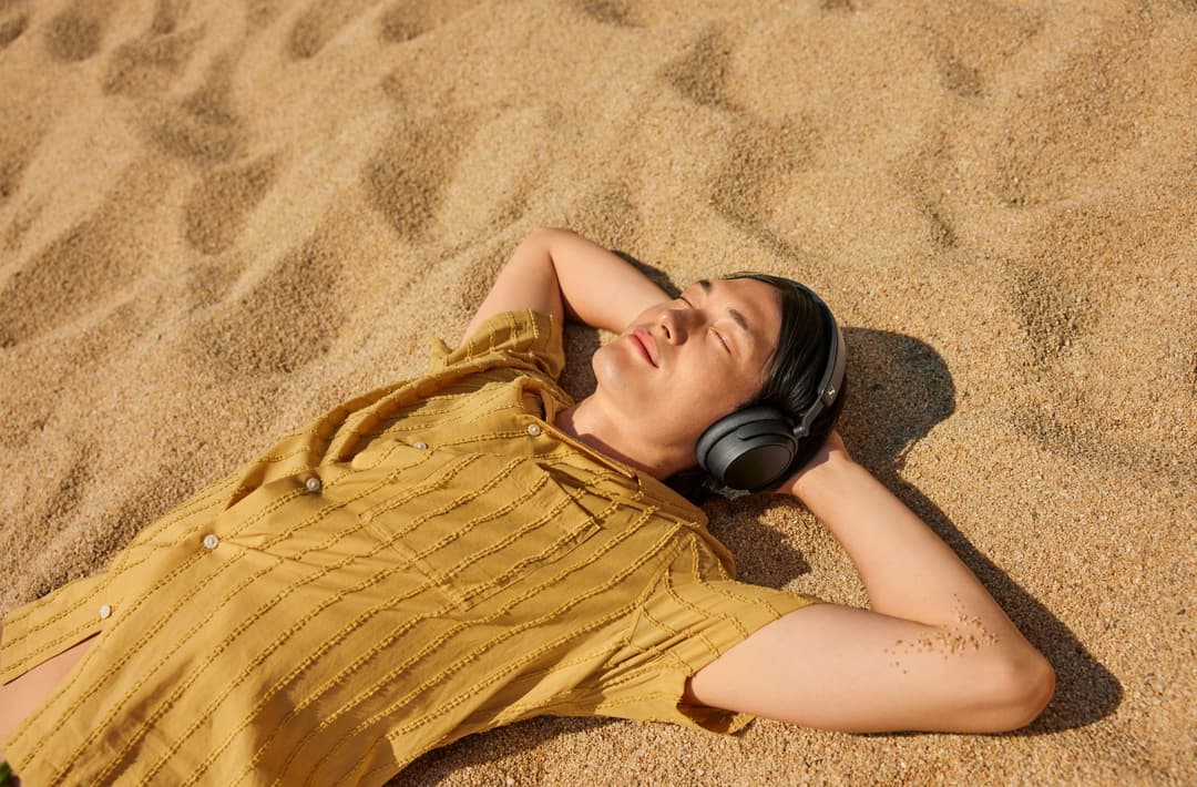 Femme allongée sur le sable portant des écouteurs Sennheiser noirs et une chemise jaune