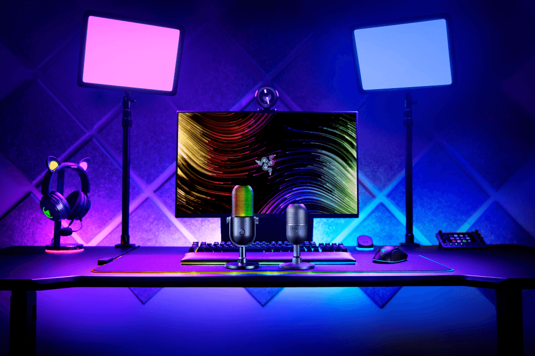 Microphones Razer Seiren V3 Mini sur un bureau gaming éclairé en violet et bleu, avec écran, casque et clavier
