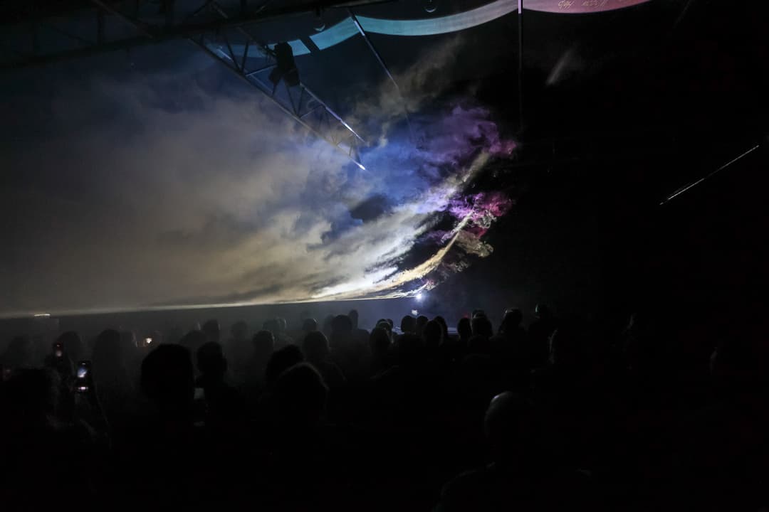 Spectacle lumineux et sonore du festival Usinesonore avec des projections bleues et violettes dans le ciel, public en silhouette au premier plan