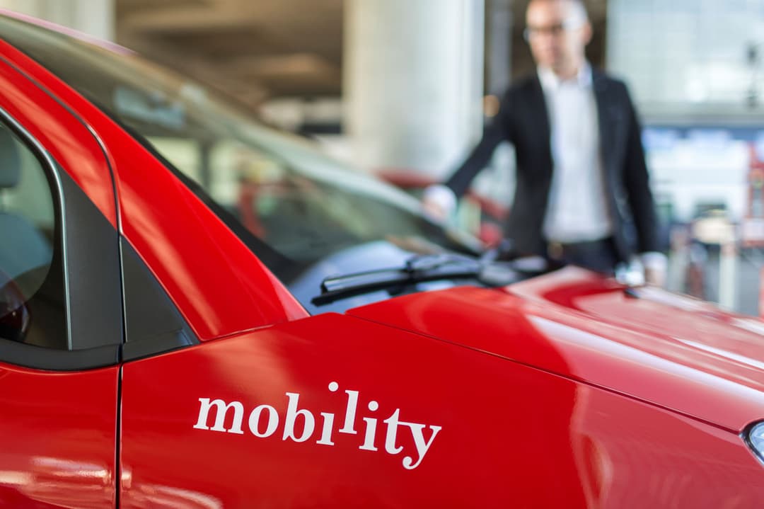 Voiture rouge de car sharing Mobility dans un parking, avec un homme en arrière-plan