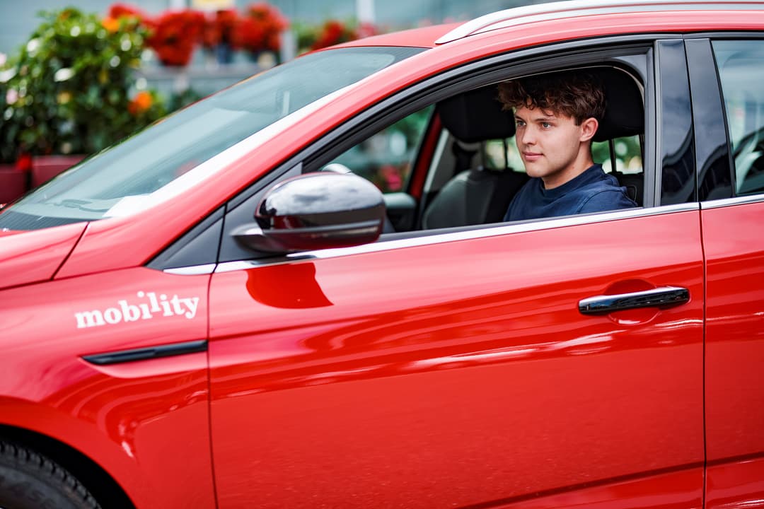 Jeune homme au volant d'une voiture rouge Mobility en milieu urbain