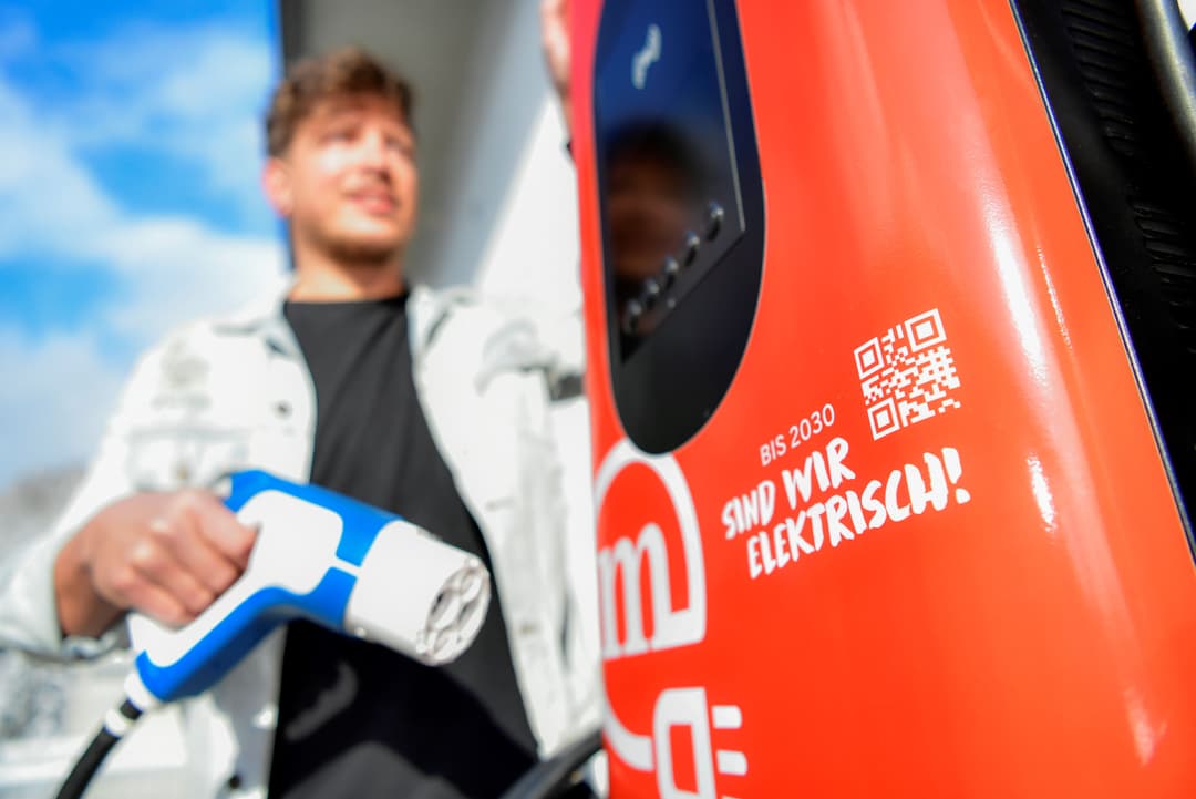 Jeune homme branchant une voiture électrique rouge sur une station de recharge, avec un QR code visible sur le véhicule