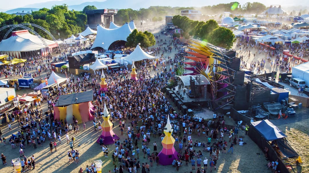 Aérienne du Paléo Festival avec foules de festivaliers, scènes colorées et tentes blanches dispersées dans le site