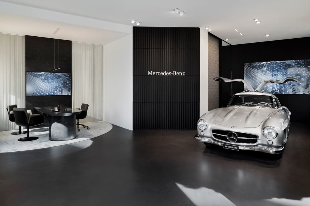 Showroom Stars@Mercedes-Benz à Zurich avec une Mercedes 300 SL classique argentée, espace épuré aux murs noirs et blancs, écrans numériques et zone de détente