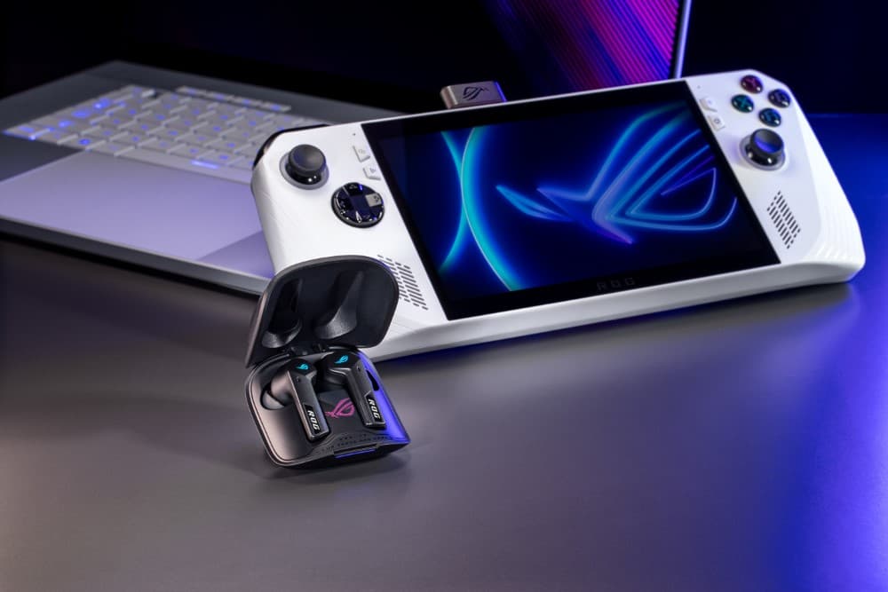 Écouteurs ROG Cetra True Wireless SpeedNova noirs et blancs avec boîtier de charge, posés devant une console de jeu portative blanche et un ordinateur portable