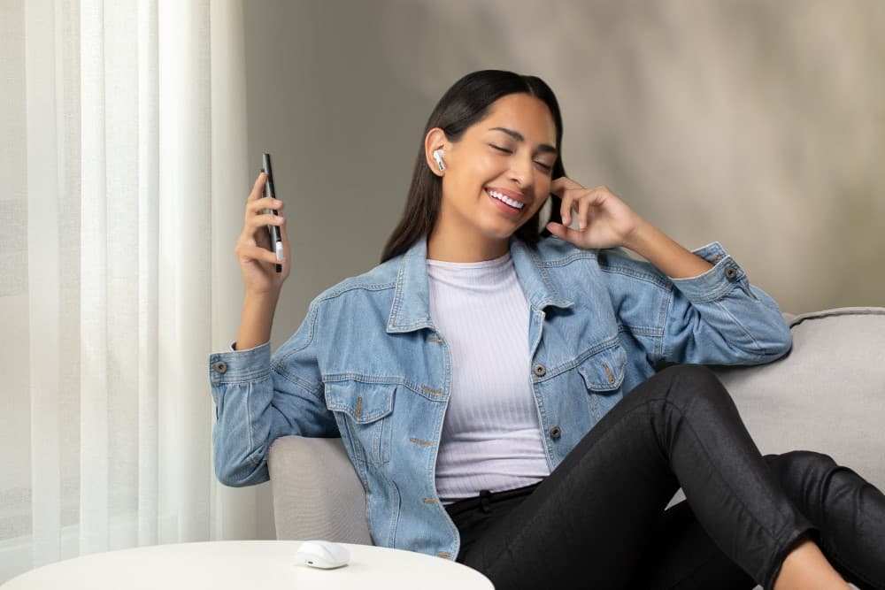 Femme portant les écouteurs ASUS ROG Cetra True Wireless SpeedNova, assise sur un canapé gris et tenant un téléphone à la main