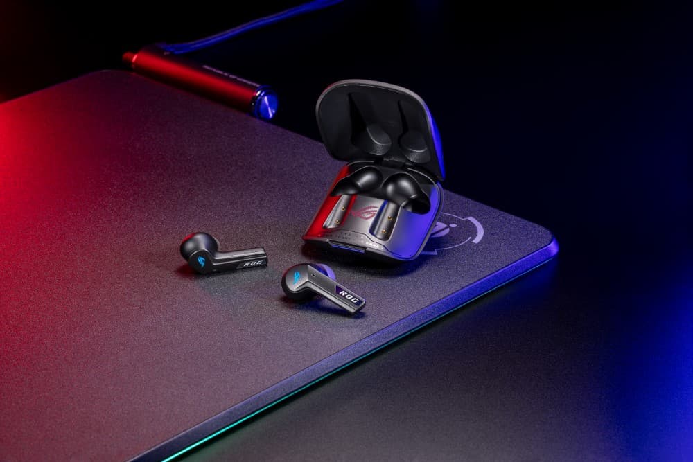 Écouteurs ASUS ROG Cetra True Wireless SpeedNova noirs avec étui de charge ouvert, posés sur un tapis gaming éclairé en rouge et bleu