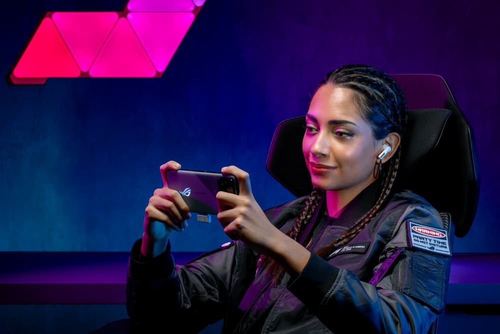 Gamer tenant un smartphone ASUS ROG avec écouteurs Cetra True Wireless, éclairage RGB magenta et bleu en arrière-plan