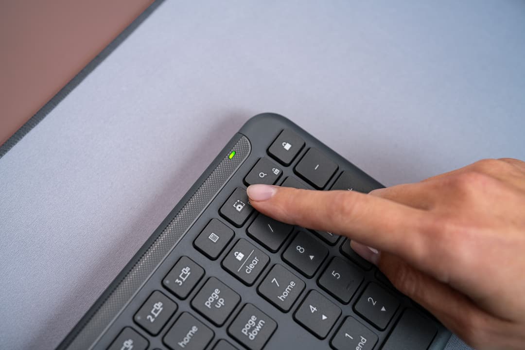 Clavier Logitech Signature Slim K950 gris graphite avec une main posée dessus, sur un bureau