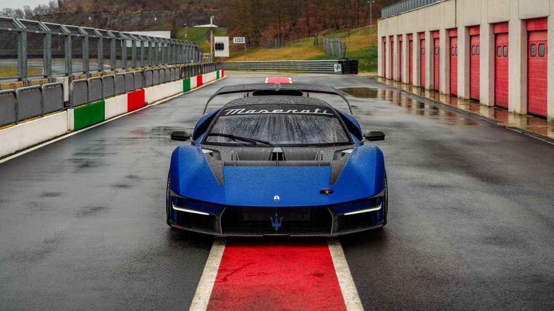 Maserati MCXtrema bleue de face sur la piste mouillée de l'Autodromo Varano de' Melegari, bordée par les murets aux couleurs italiennes
