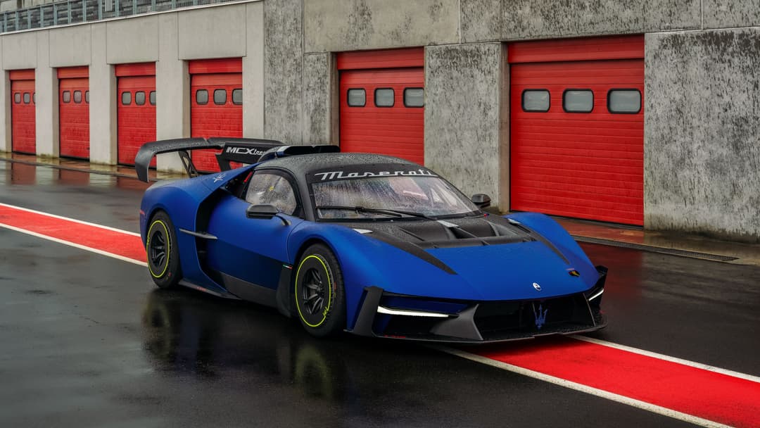 Maserati MCXtrema bleu et noir en piste devant des portes de garage rouges, avec aileron carbone et jantes jaunes