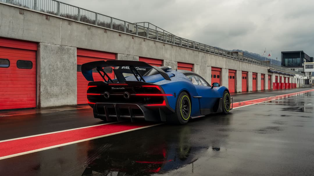 Maserati MCXtrema bleu et noir vue de trois quarts arrière sur un circuit, garages rouges en arrière-plan