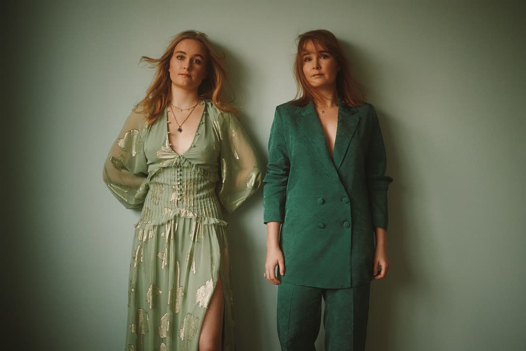 Hannah-Leah et Meghan des Woodgies posent côte à côte, l'une en robe pailletée vert clair, l'autre en costume vert émeraude