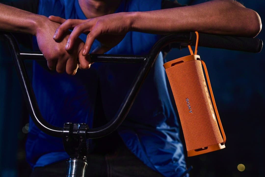 Enceinte portable Sony ULT FIELD orange et noire suspendue au guidon d'un vélo, tenue par une main en mouvement