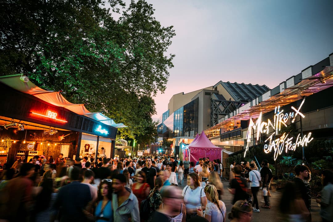 Foule de visiteurs dans les rues du Montreux Jazz Festival au crépuscule, avec enseignes lumineuses colorées et architecture urbaine