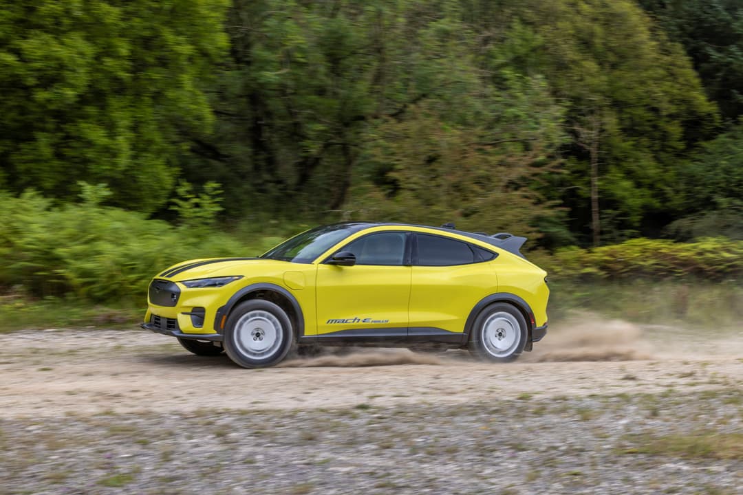 Ford Mustang Mach-E Rally jaune vif en mouvement sur terrain rocheux, entourée de végétation verte