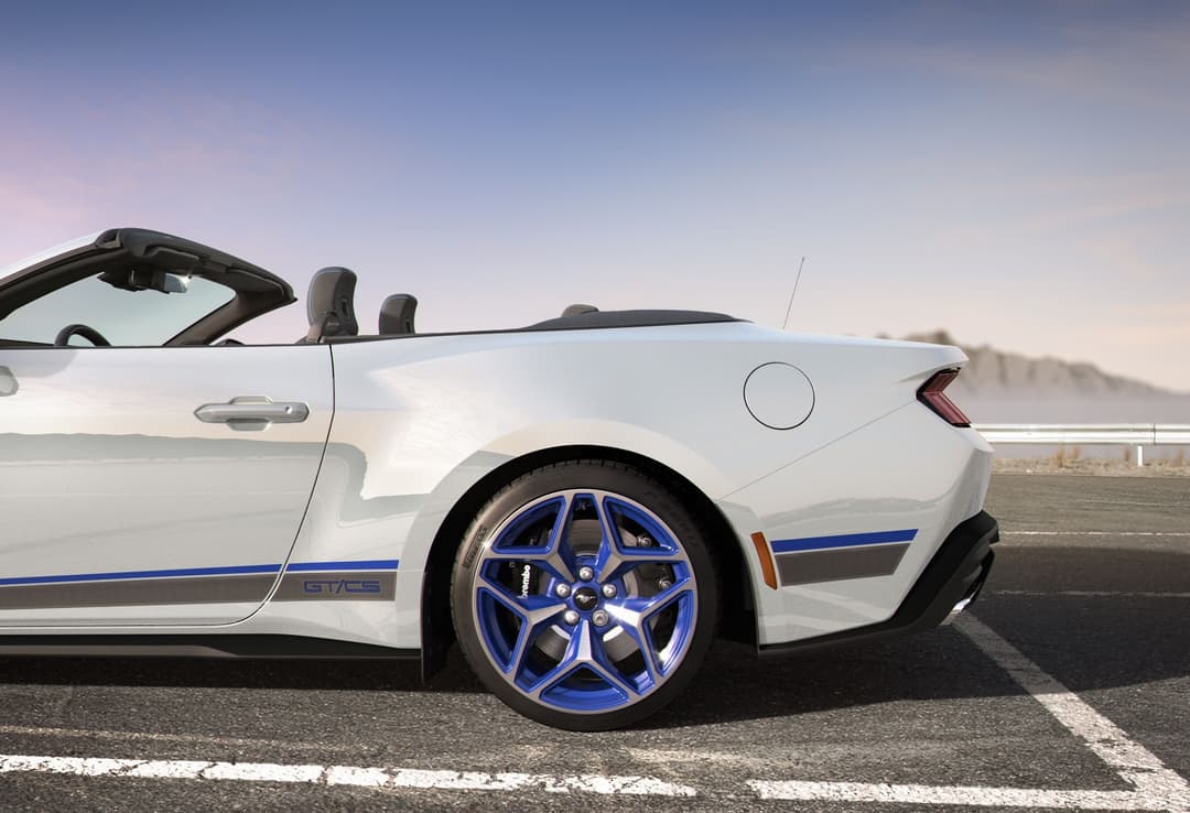 Ford Mustang GT Convertible California Special blanche avec surpiqûres bleu et gris, capote ouverte, jantes bleues, stationnée sur un circuit