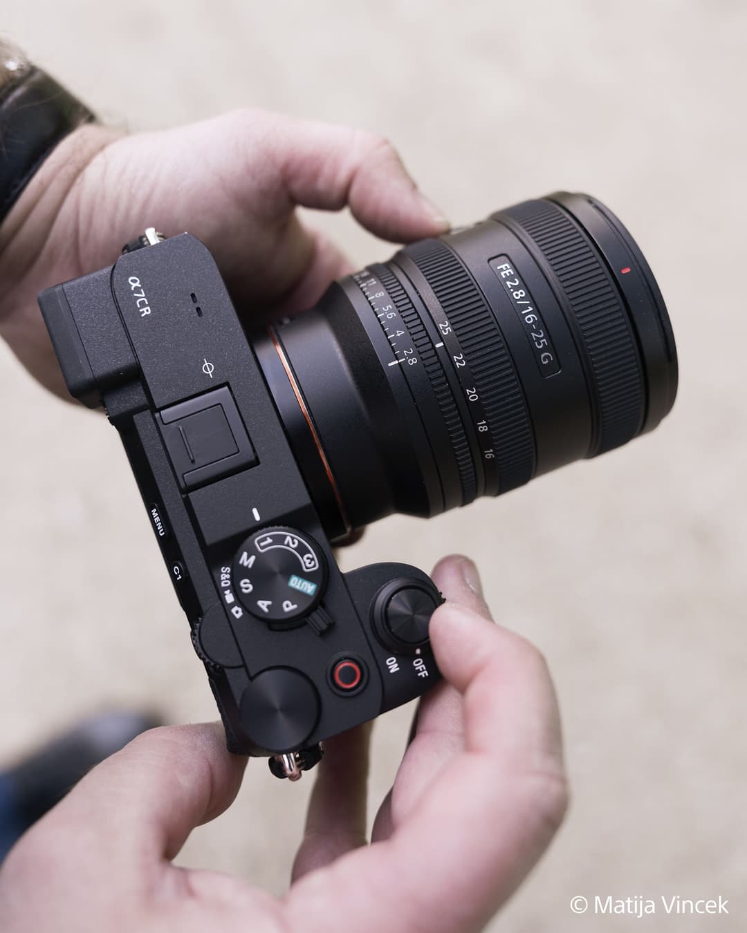 Objectif Sony FE 16-25mm F2.8 G monté sur un boîtier noir tenu à deux mains, vue de trois-quarts