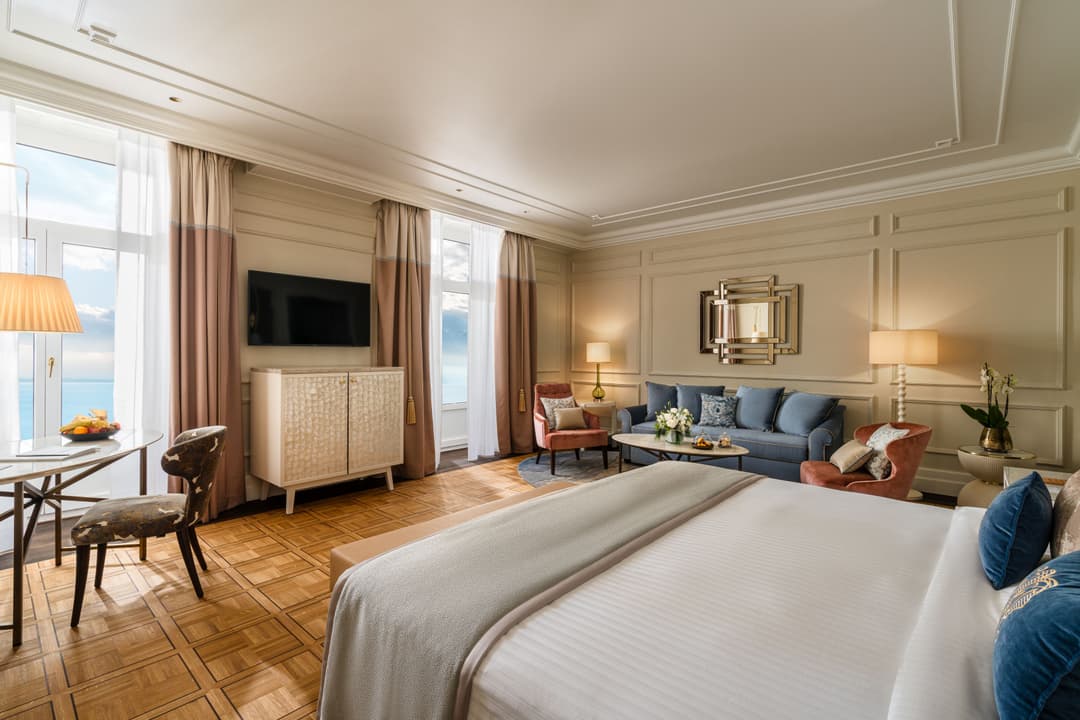 Chambre rénovée du Fairmont Le Montreux Palace avec lit, salon, vue sur le lac et décoration aux tons beige et bleu