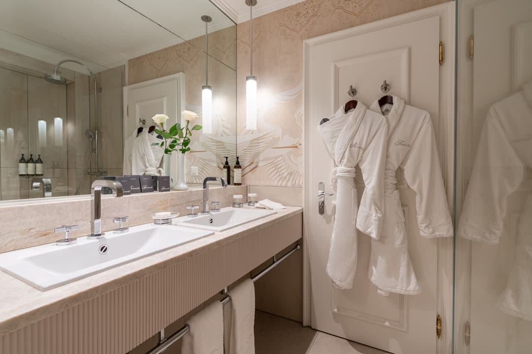 Salle de bain rénovée du Fairmont Le Montreux Palace avec double vasque, papier peint à motifs naturels et peignoirs blancs