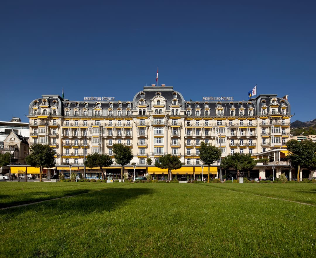 Fairmont Le Montreux Palace, imposant hôtel Belle Époque aux façades blanche et dorée, avec toits mansardés, vu depuis une pelouse verte