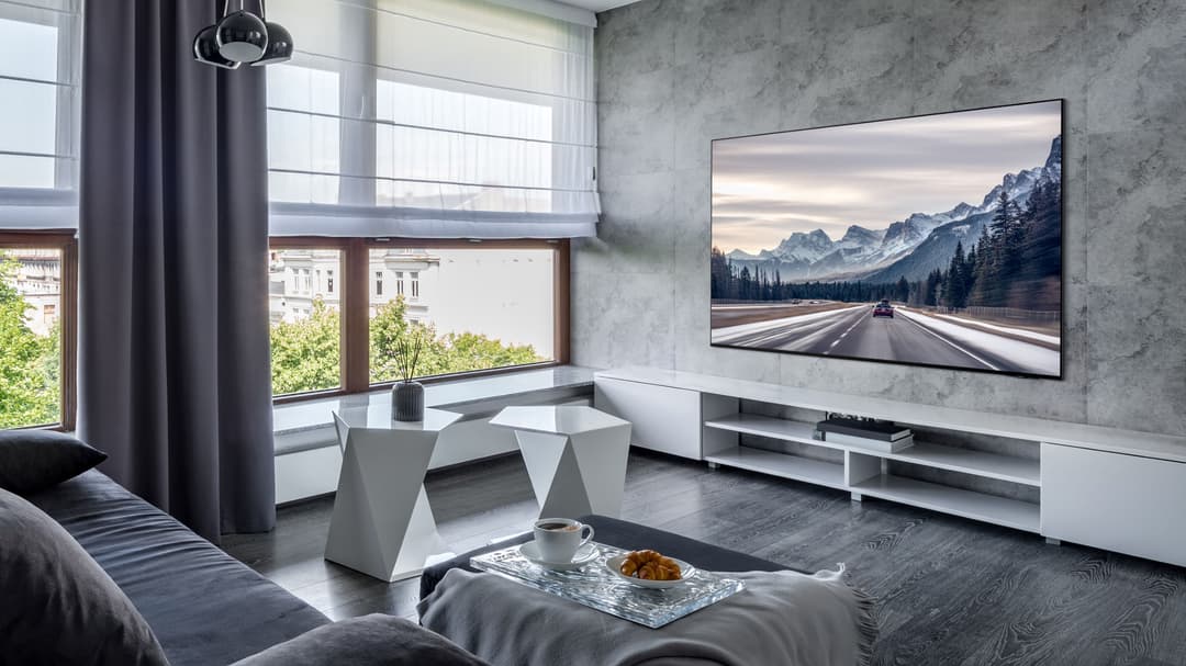 Téléviseur Samsung Neo QLED 8K affichant un paysage montagneux, accroché au mur d'un salon moderne aux tons gris et blanc