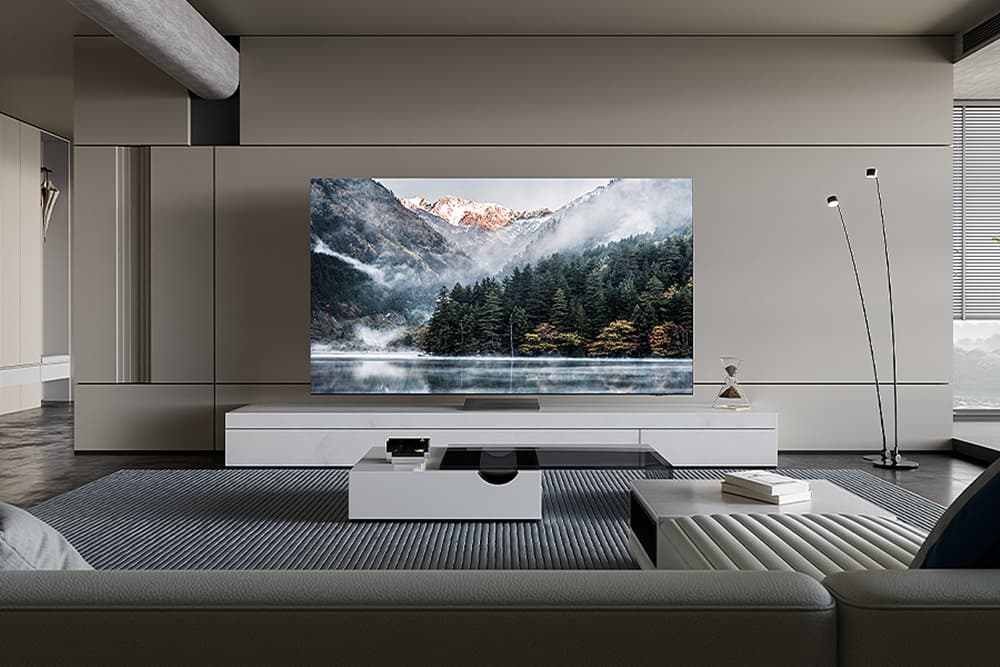 Samsung AI TV affichant un paysage montagneux avec lac et forêts, installée dans un salon minimaliste aux tons gris et blanc