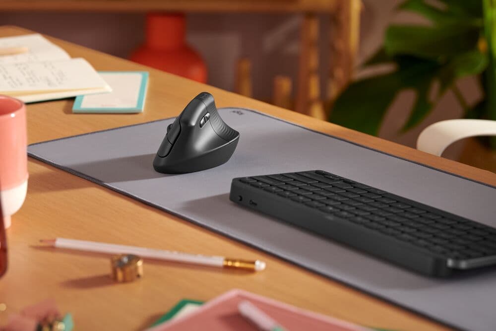 Clavier ergonomique noir Logitech ERGO et souris verticale noire sur un tapis gris, posés sur un bureau en bois