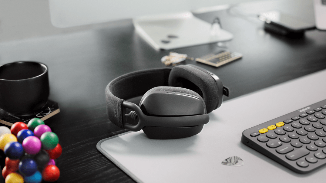 Casque supra-auriculaire Logitech Zone Vibe noir posé sur un bureau avec clavier, souris et accessoires