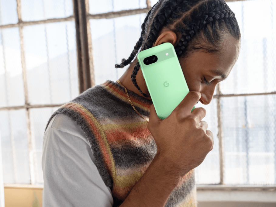 Personne tenant un Pixel 8a vert clair près de son oreille, avec une fenêtre lumineuse en arrière-plan