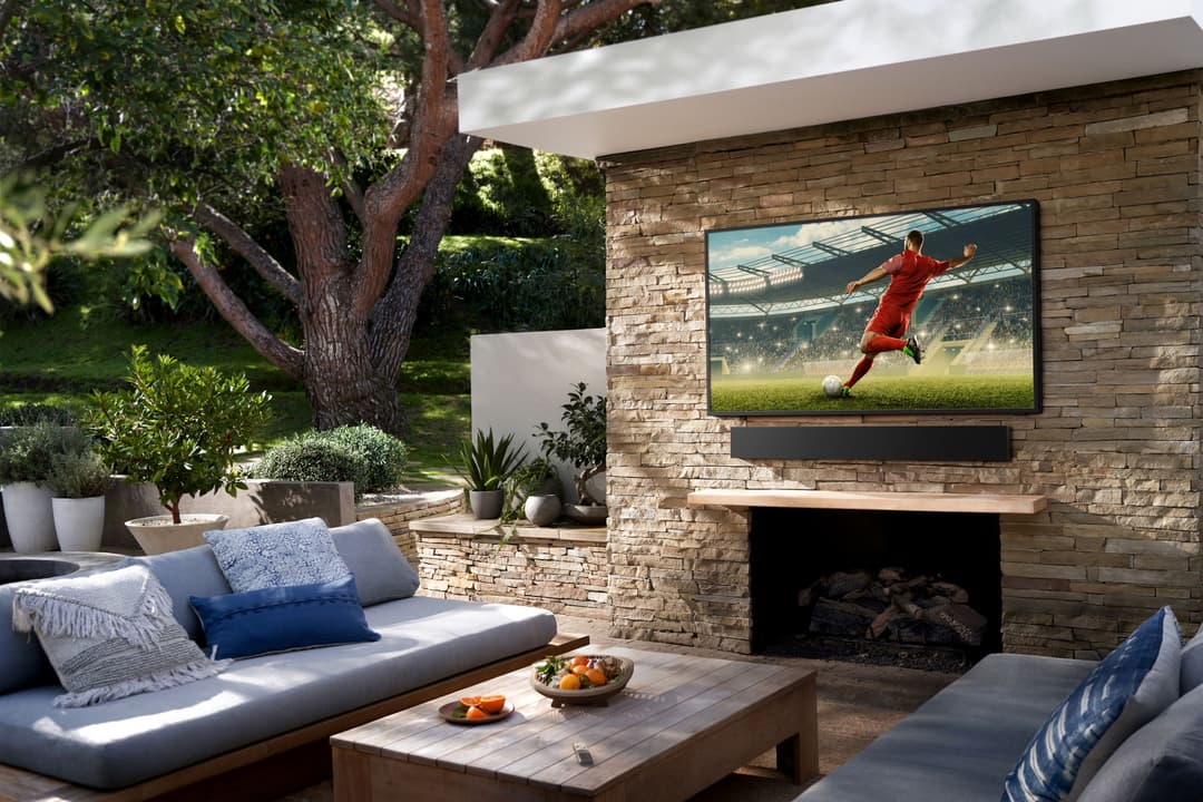 Téléviseur Samsung affichant un joueur de football en rouge dans un stade, installé dans un salon de jardin avec foyer