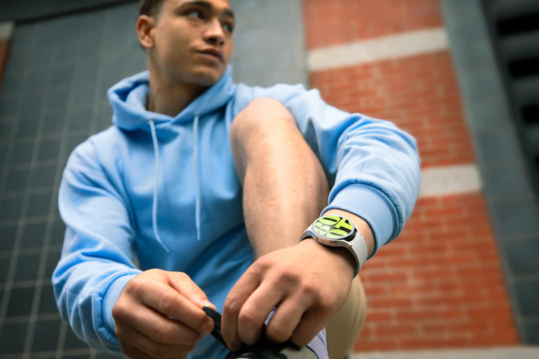 Jeune homme en sweatshirt bleu portant une montre connectée Samsung au poignet