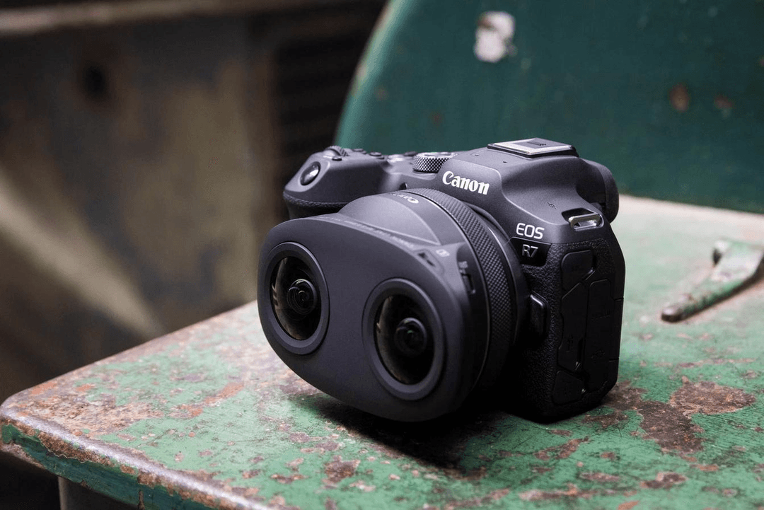Appareil photo Canon EOS R équipé du nouvel objectif RF-S 3.9mm F3.5 STM DUAL FISHEYE avec ses deux lentilles côte à côte, posé sur une surface verte oxydée