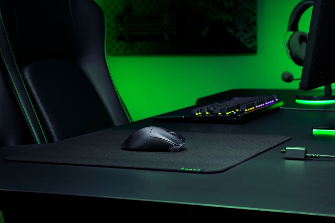 Souris Razer DeathAdder V3 HyperSpeed noire sur tapis de souris gris dans un setup gaming illuminé de vert