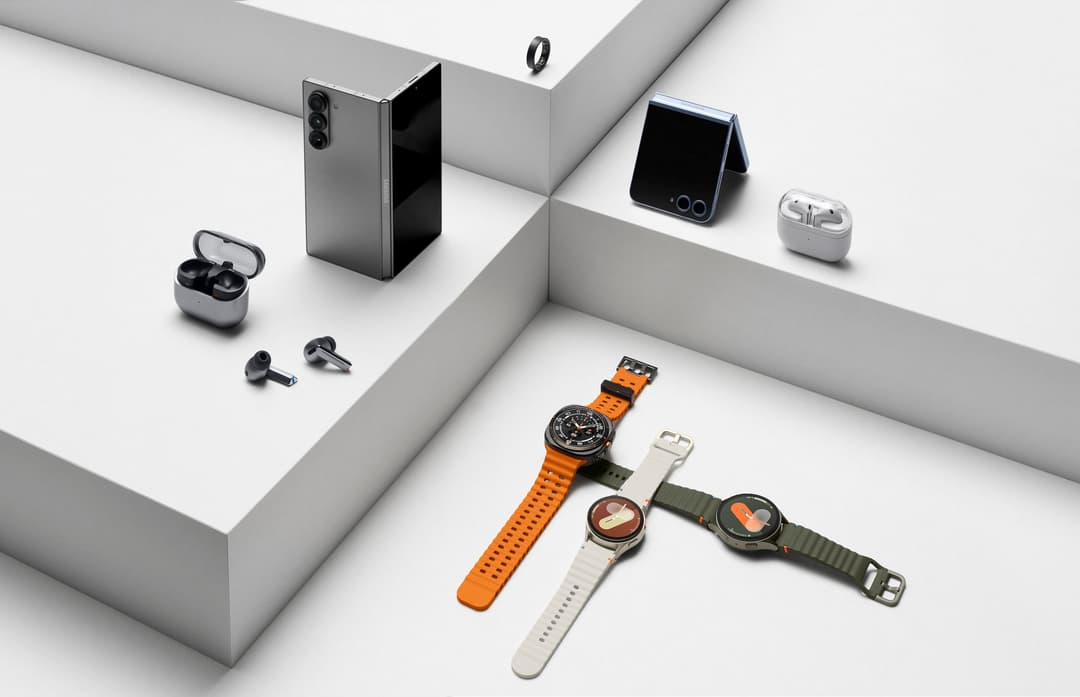 Galaxy Ring noir en haut, Galaxy Buds3 et Buds3 Pro gris et blancs, smartphone plié gris, et trois montres Galaxy Watch avec bracelets orange, blanc et kaki