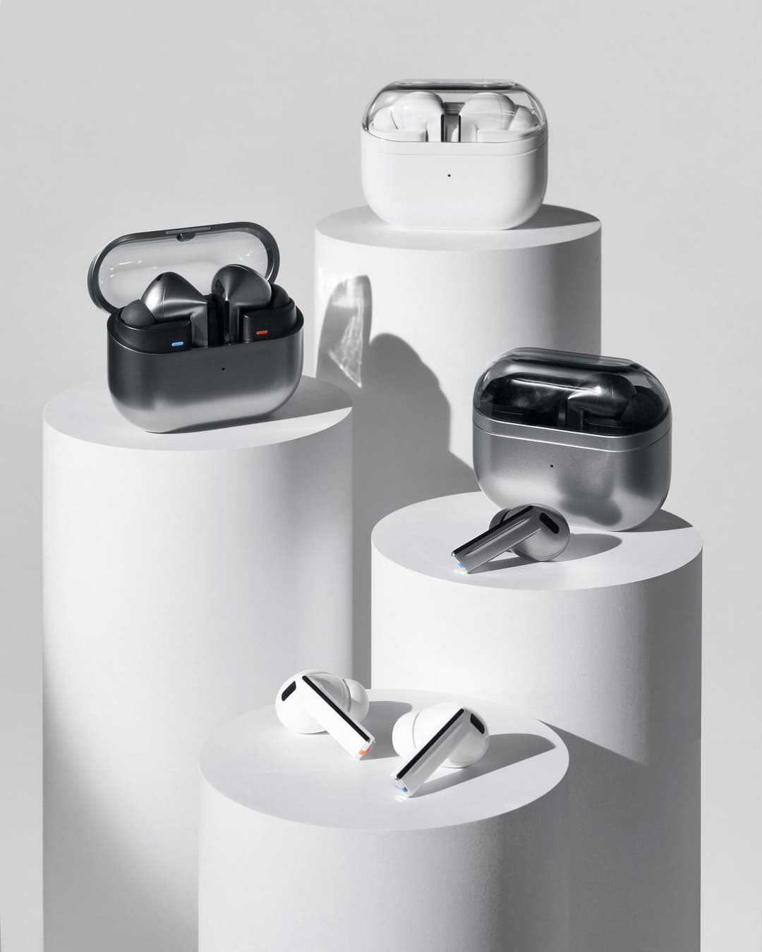 Quatre modèles de Galaxy Buds3 présentés sur des socles blancs : boîtiers noirs et blancs, écouteurs blancs et noirs avec indicateurs lumineux colorés