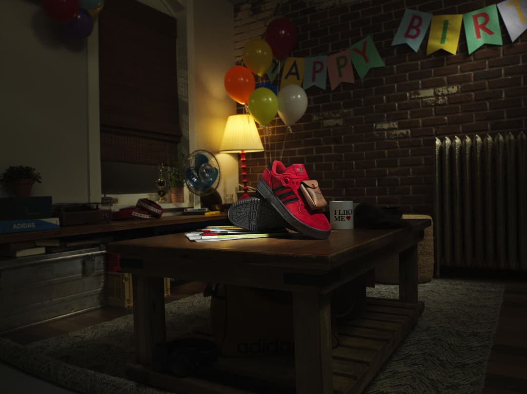 Sneaker Adidas rouge et noire posée sur un bureau en bois, dans une ambiance festive avec ballons et guirlande « Happy Birthday »