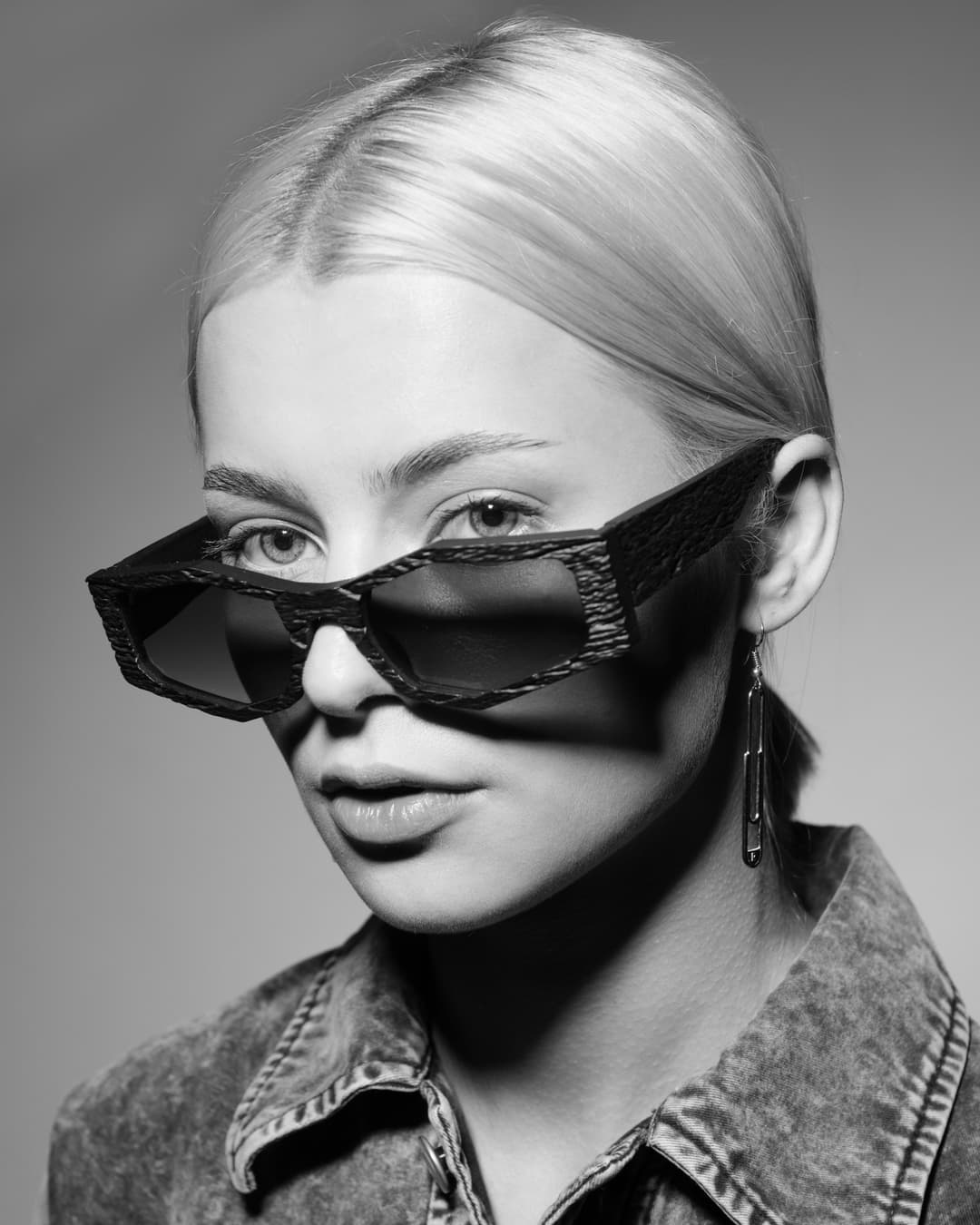 Femme portant des lunettes VISAGES® aux verres noirs surdimensionnés et monture texturée, photographie en noir et blanc