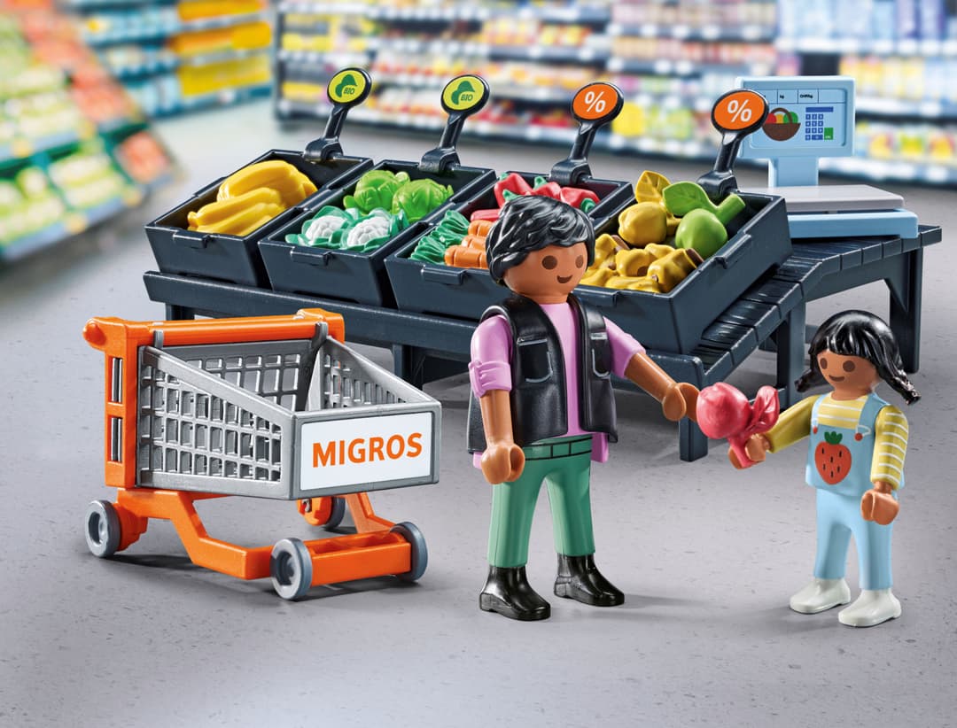 Figurines PLAYMOBIL au rayon fruits et légumes Migros avec chariot d'achat orange, vendeur en gilet rose et enfant en blouse bleue