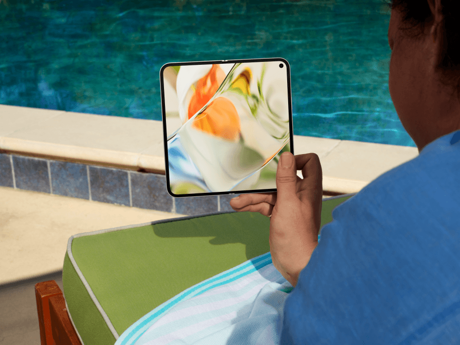 Pixel 9 Pro Fold tenu à la main près d'une piscine, écran allumé affichant une image colorée clairement visible en plein soleil