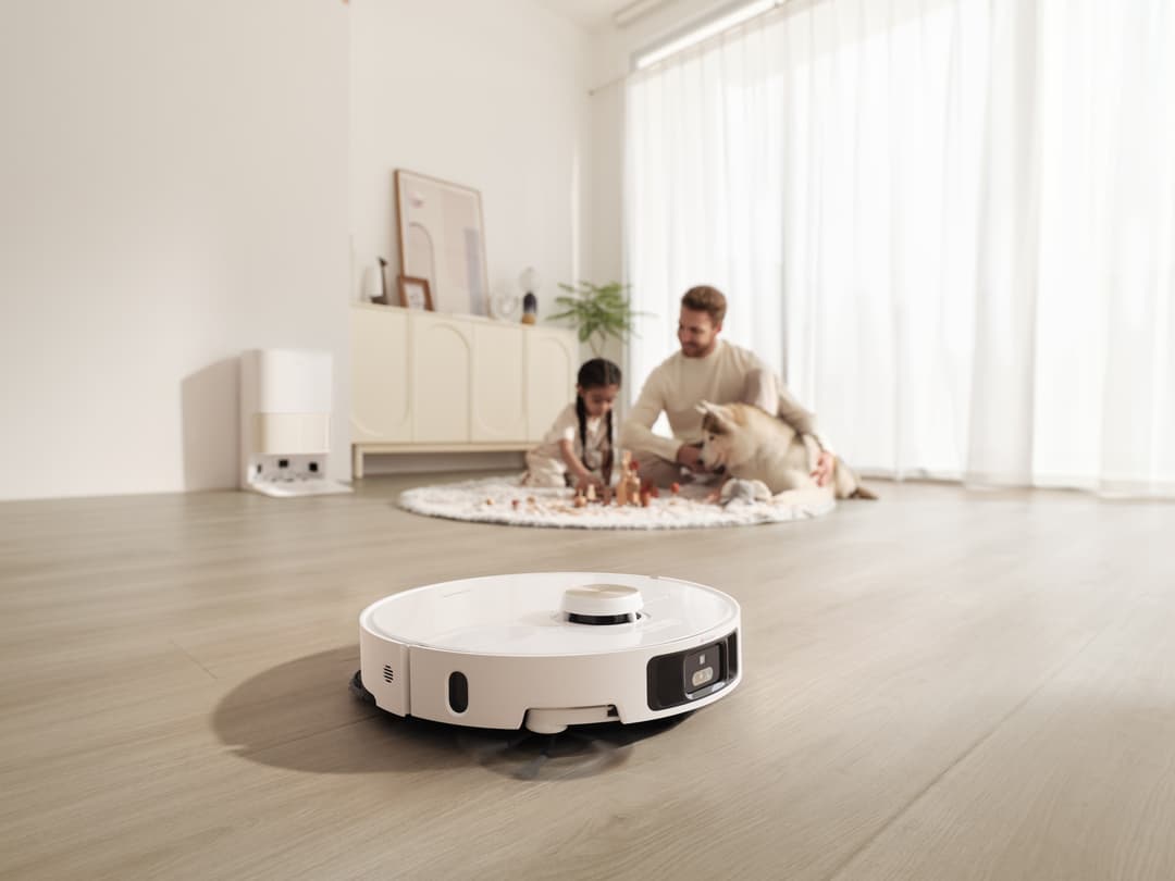 Robot aspirateur Dreame L40 Ultra blanc et noir circulant sur un parquet, famille et chien en arrière-plan dans un salon
