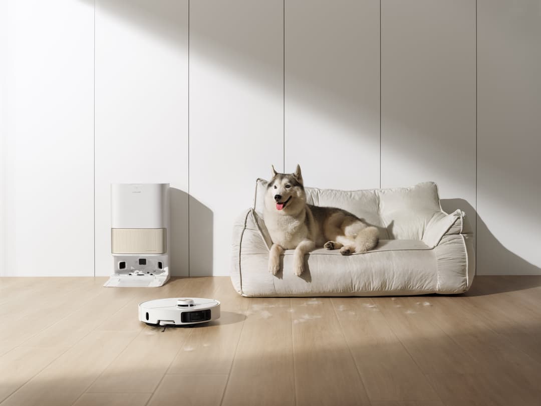 Robot aspirateur Dreame L40 Ultra blanc circulant sur un parquet clair près d'un canapé où repose un husky