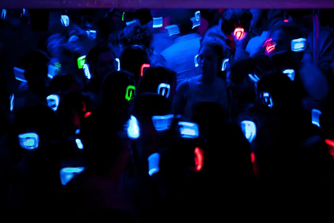 Foule dansant dans une discothèque avec lumières néon bleu, rouge et vert, nombreux téléphones levés dans la nuit