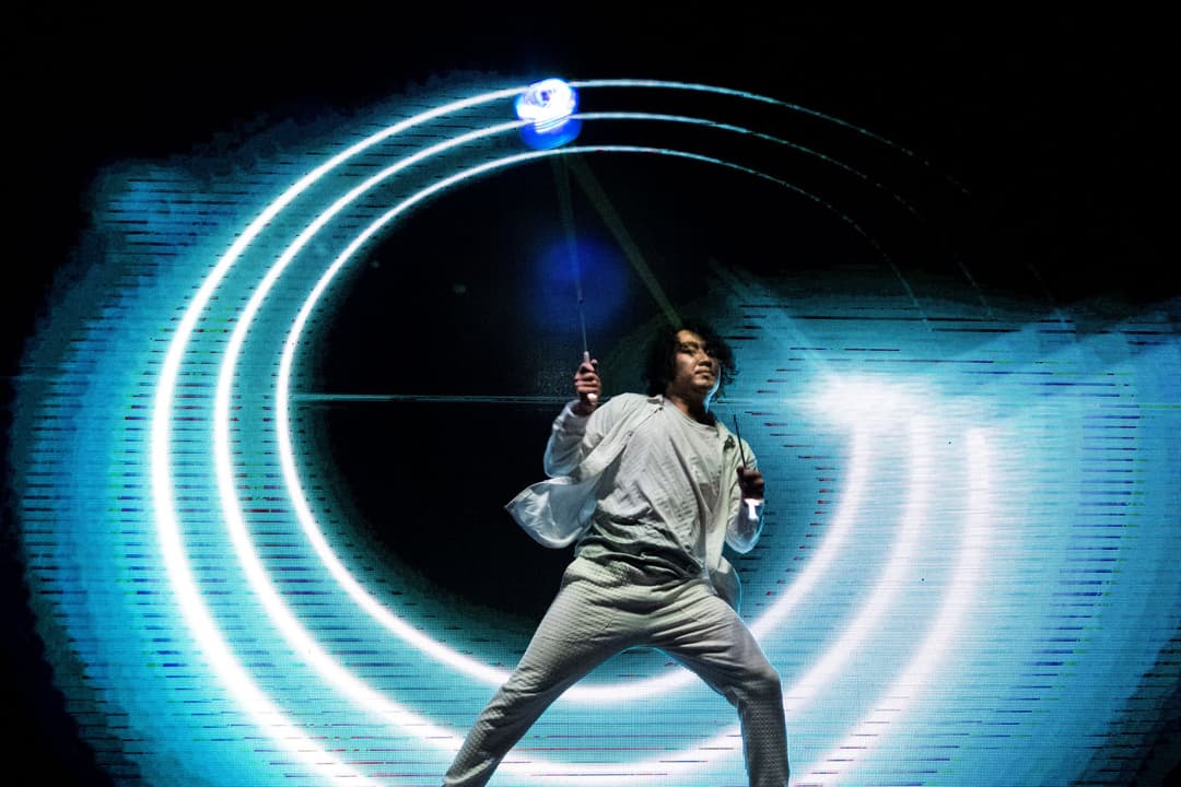 Mochi, artiste japonais, en action sur scène avec un contrôleur de jeu, entouré de néons bleus luminescents