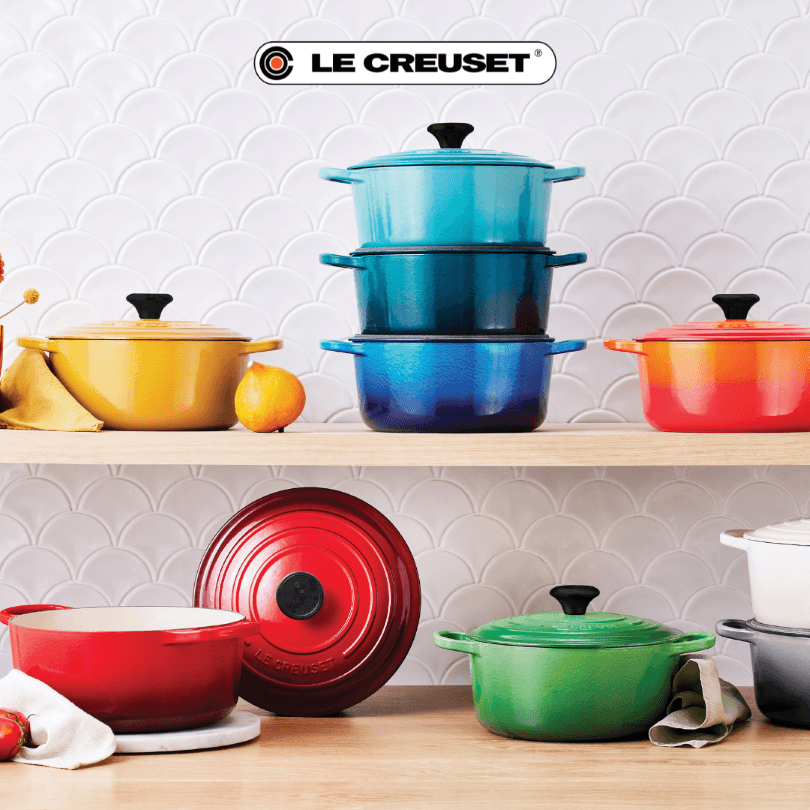 Logo Le Creuset avec batteries de cuisine colorées empilées sur deux étagères : jaune, bleu dégradé et rouge-orange, posées sur fond blanc