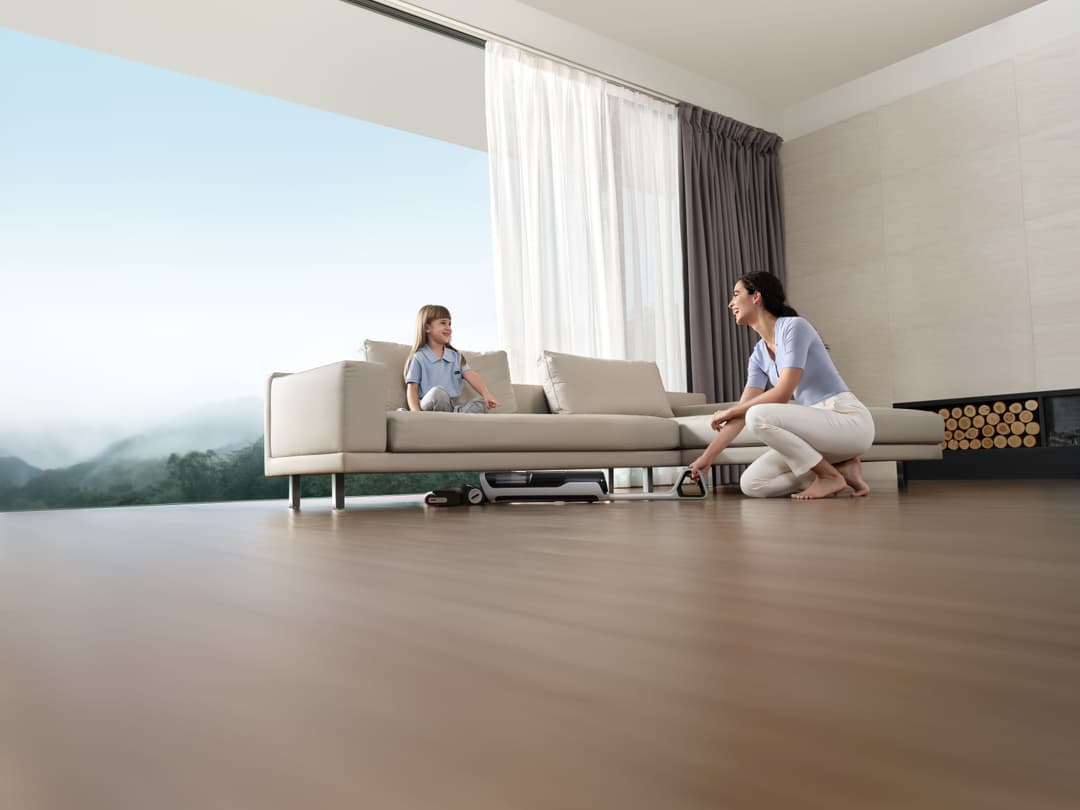 Aspirateur Dreame H14 Pro sous un canapé dans un salon moderne, femme et enfant observant le nettoyage du sol